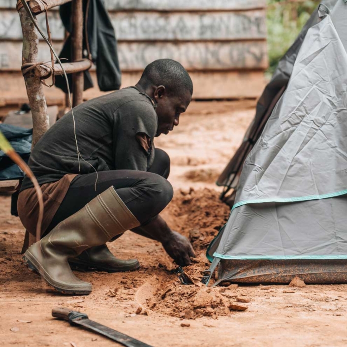 A behind the scenes photo of a community member digging a trench to protect his tent from the rain. Photo taken for the short film Ikouah: Into The Heart Of Cameron's Rainforest, created by Videographer Jack Dunn for Videography portfolio